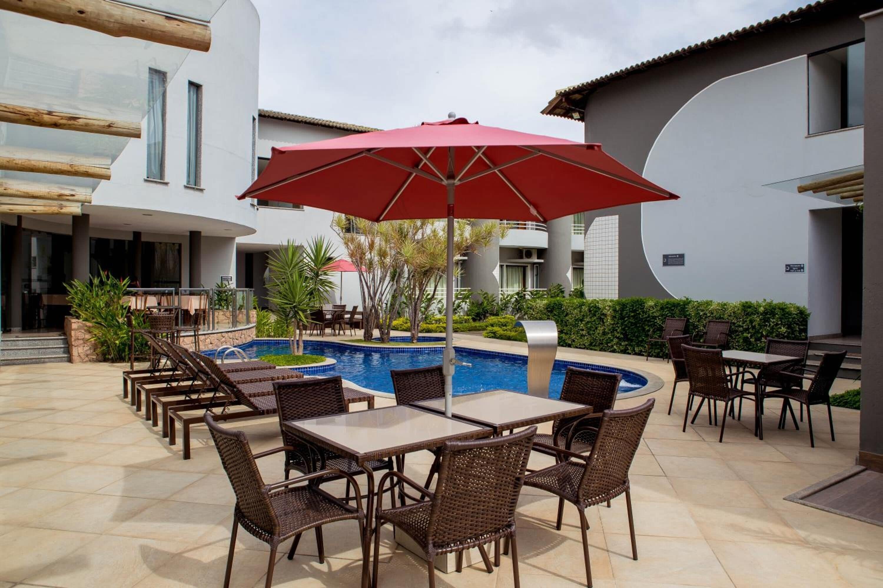 A poolside area with outdoor seating and a red umbrella.