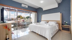 A modern hotel room with a large bed, a desk with a computer, and a balcony with a view of the city. - Hotel Porto Nápolis (Eunapolis)