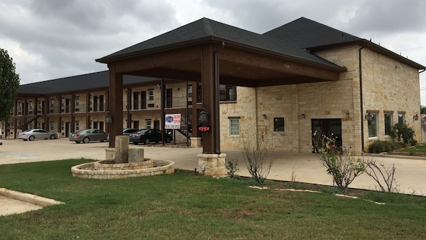 A two-story building with a stone facade, a covered entrance, and a parking lot with several cars. - Pearsall Inn & Suites (Pearsall)