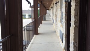 A covered corridor with stone walls, a concrete floor, and a railing on one side. - Pearsall Inn & Suites (Pearsall)