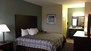 A hotel room with a bed, a desk, a chair, a lamp, a phone, a mirror, and a picture on the wall. - Pearsall Inn & Suites (Pearsall)