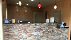 A reception area with a stone wall, a counter, and a door. - Pearsall Inn & Suites (Pearsall)