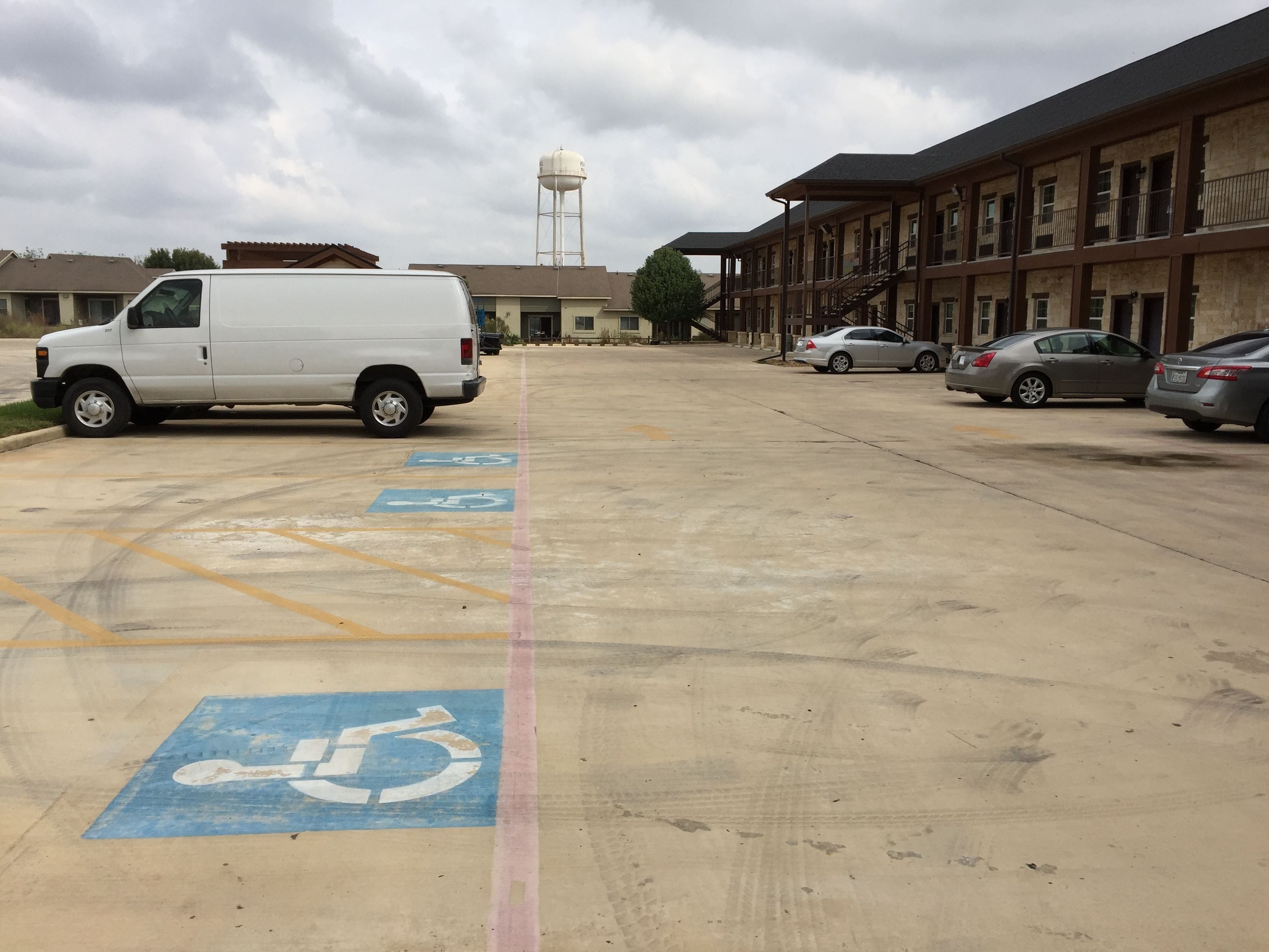 Un estacionamiento con espacios reservados para personas con movilidad reducida, una camioneta blanca y varios automóviles estacionados.