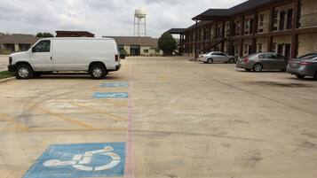 A parking lot with designated handicapped spaces, a white van, and several cars parked.