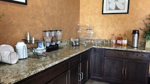 A kitchen with granite countertops, dark wooden cabinets, a coffee station, and a framed abstract artwork on the wall. - Pearsall Inn & Suites (Pearsall)