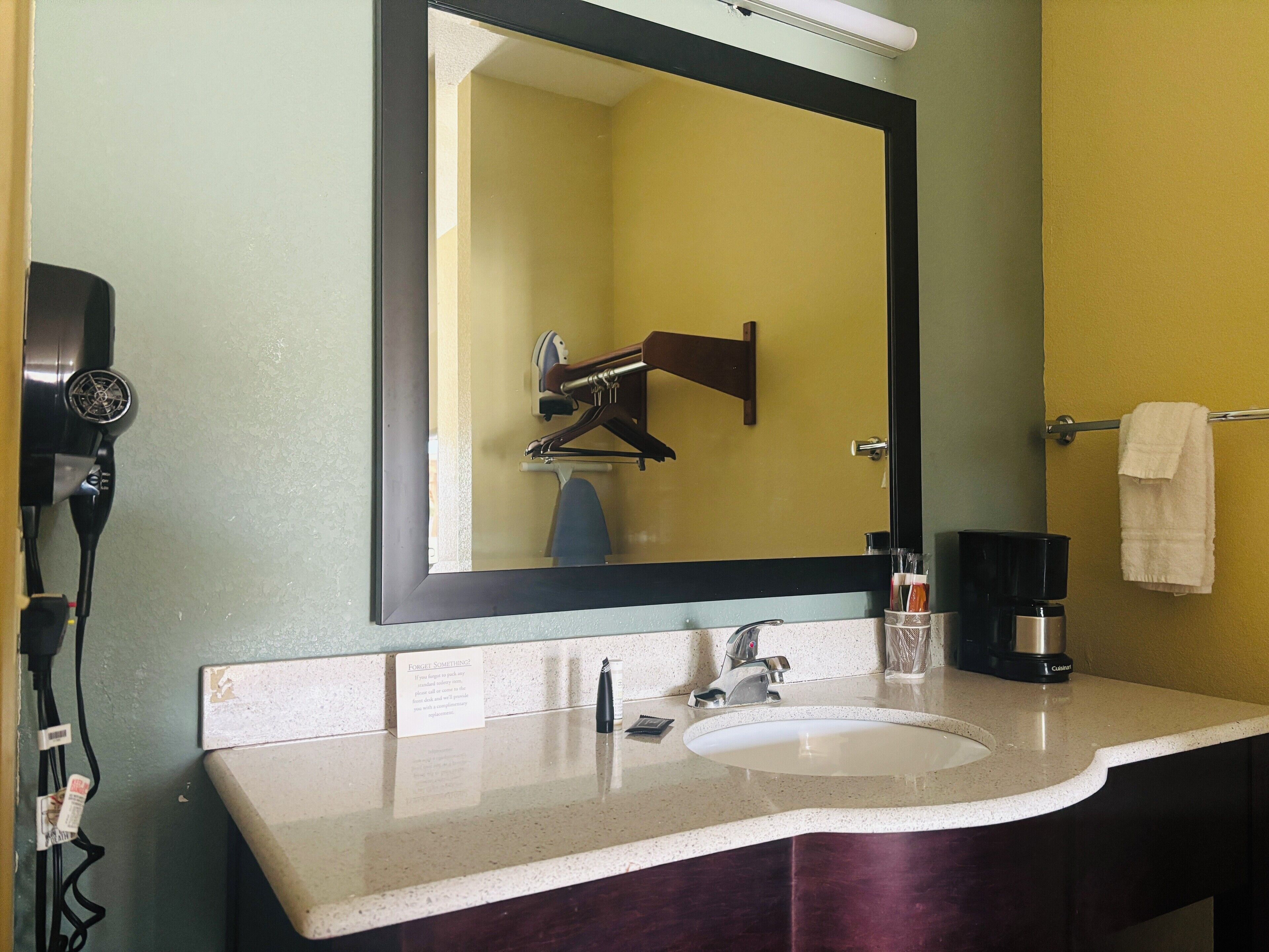A bathroom with a sink, mirror, towel rack, and a hairdryer on the wall.