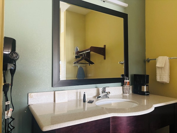 A bathroom with a sink, mirror, towel rack, and a hairdryer on the wall. - Pearsall Inn & Suites (Pearsall)