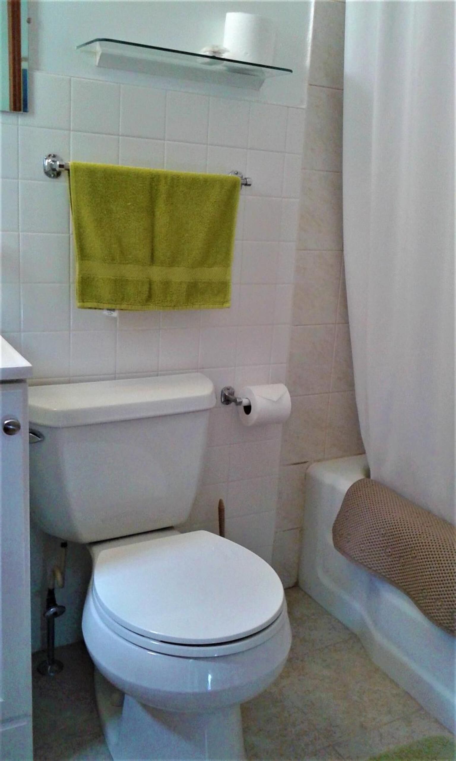 A bathroom with a white toilet, a green towel hanging on the wall, and a shower curtain.