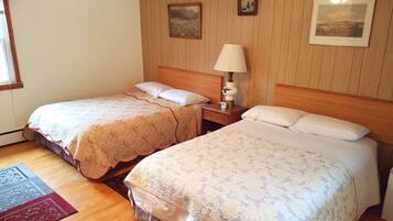 Habitación de hotel con dos camas, cabeceros de madera, una mesita de noche con lámpara y dos cuadros enmarcados en la pared.