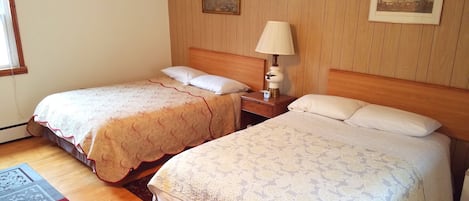 A hotel room with two beds, wooden headboards, a nightstand with a lamp, and two framed pictures on the wall.