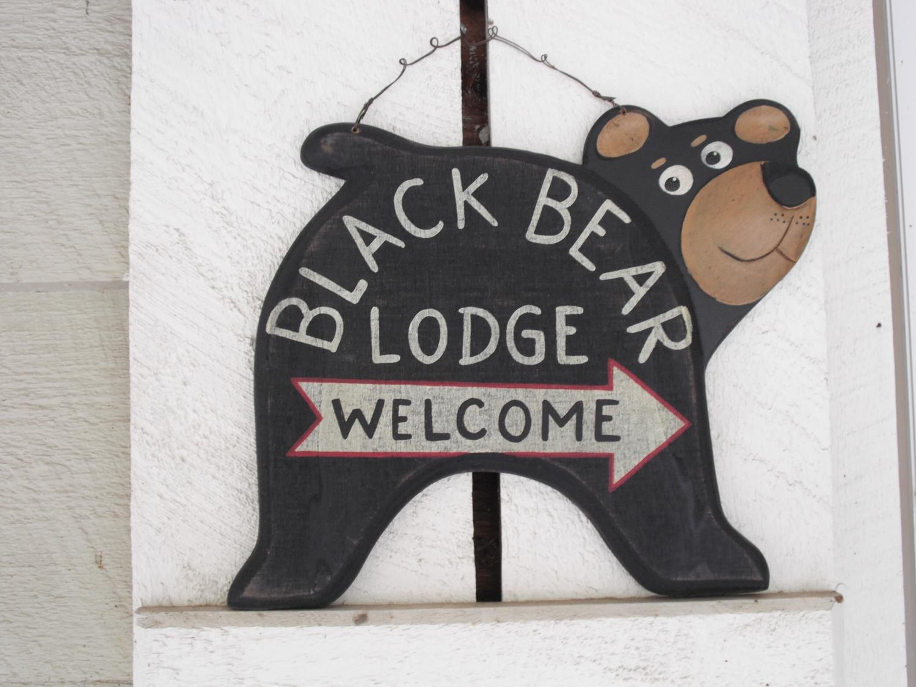 Un letrero con forma de oso negro que dice "BLACK BEAR LODGE" y una flecha de "BIENVENIDA".