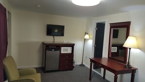 A hotel room with a flat-screen TV mounted on the wall, a minibar, a desk with a lamp, a chair, and a door. - Pleasant Hill Motel (Middletown)
