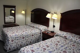 Habitación de hotel con dos camas, una mesita de noche, un espejo y dos lámparas de pared.