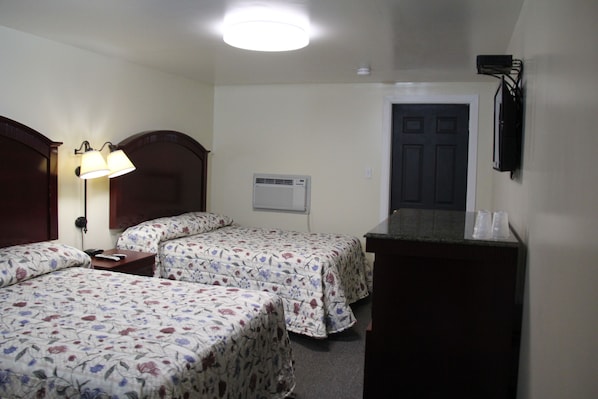 A hotel room with two beds, a desk, a lamp, an air conditioning unit, and a television mounted on the wall. - Pleasant Hill Motel (Middletown)