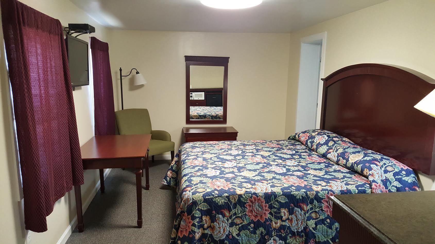 A hotel room with a bed, a desk, a chair, a TV, and a mirror.