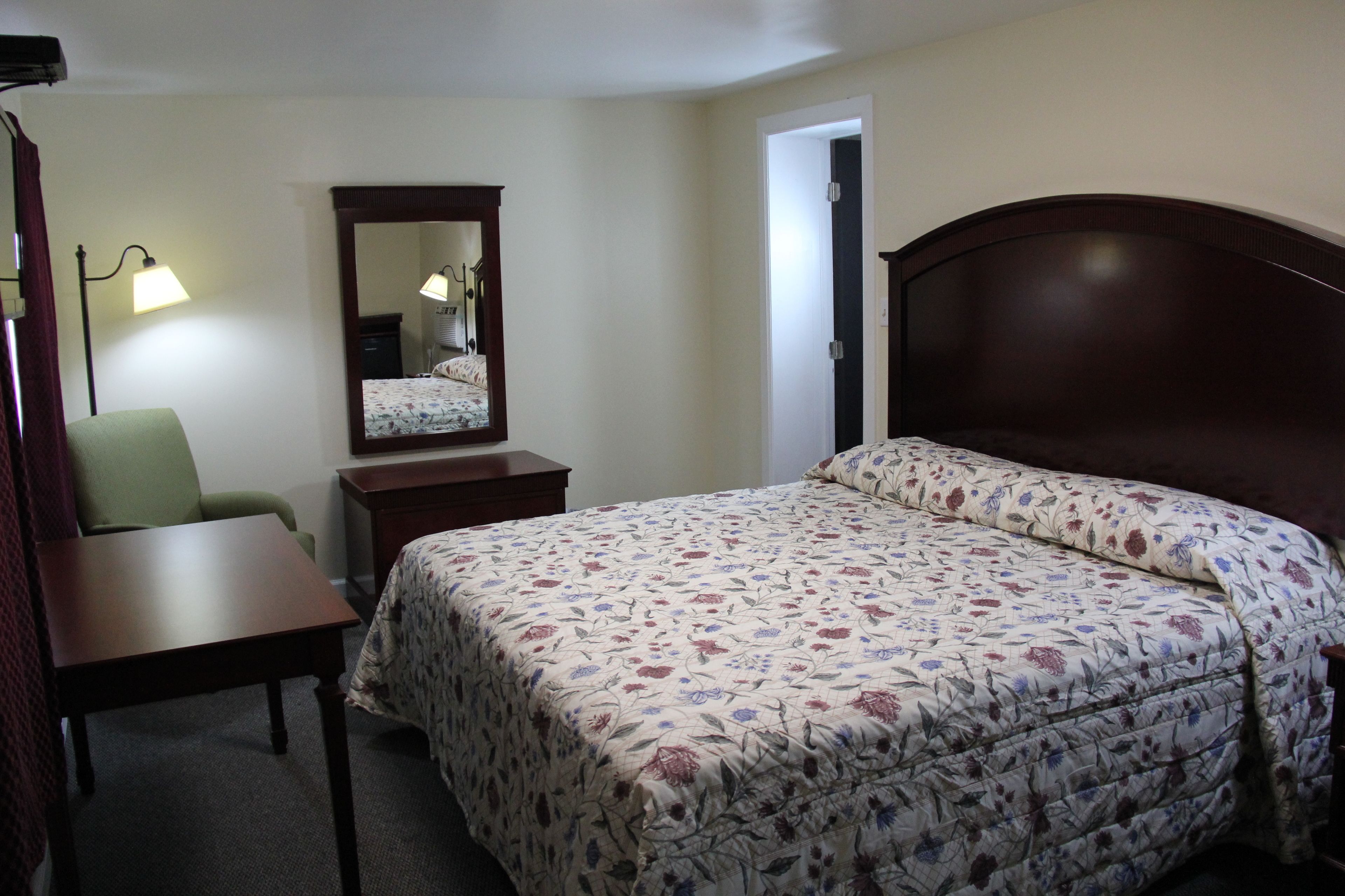 Een hotelkamer met een bed, een bureau, een stoel, een dressoir, een spiegel en een lamp.