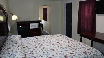 A bedroom with a floral bedspread, a bedside lamp, a dresser with a microwave, and a TV on a stand.