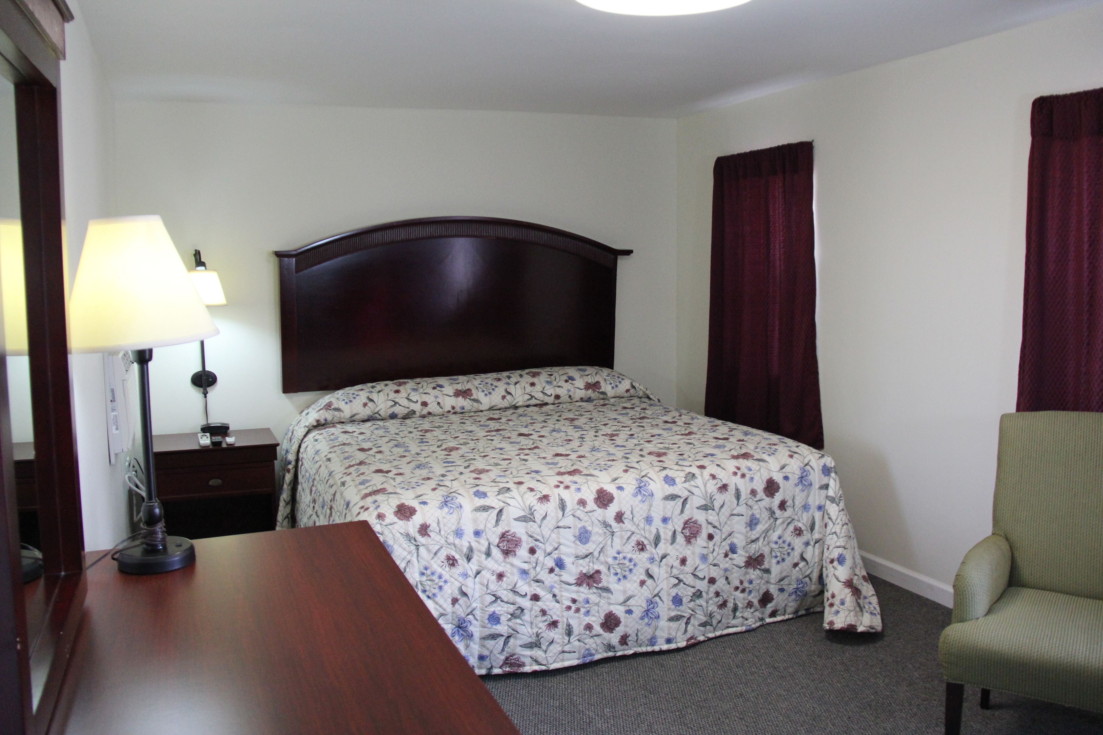 A hotel room with a bed, a desk, a chair, a lamp, and a nightstand.
