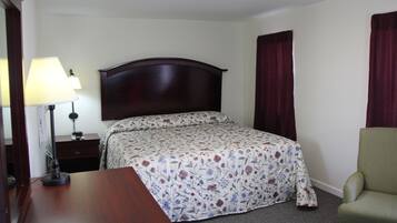 A hotel room with a bed, a desk, a chair, a lamp, and a nightstand.