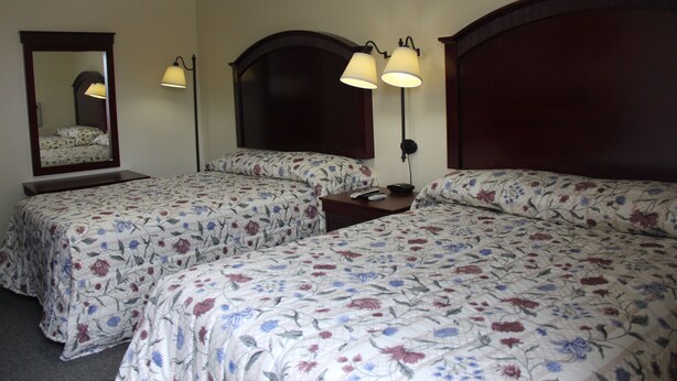 A hotel room with two beds, each with floral bedding, a large mirror, and two wall-mounted lamps. - Pleasant Hill Motel (Middletown)