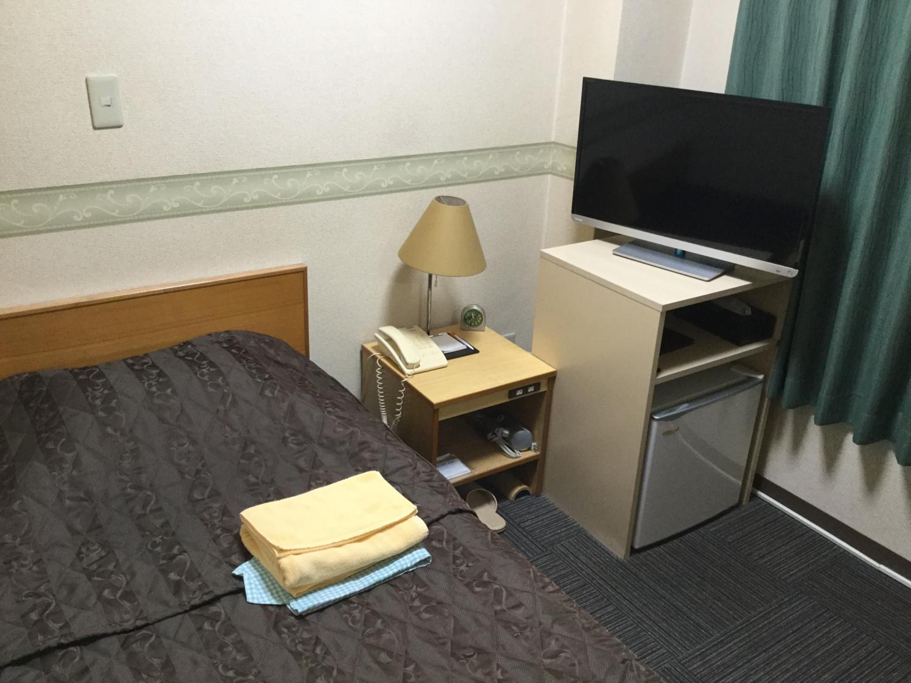 Una habitación de hotel con cama, escritorio con televisor, lámpara y refrigerador pequeño.