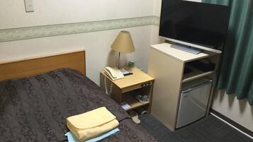 Una habitación de hotel con cama, escritorio con televisor, lámpara y refrigerador pequeño.