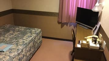 A hotel room with a bed, a desk with a computer, a telephone, and a lamp.
