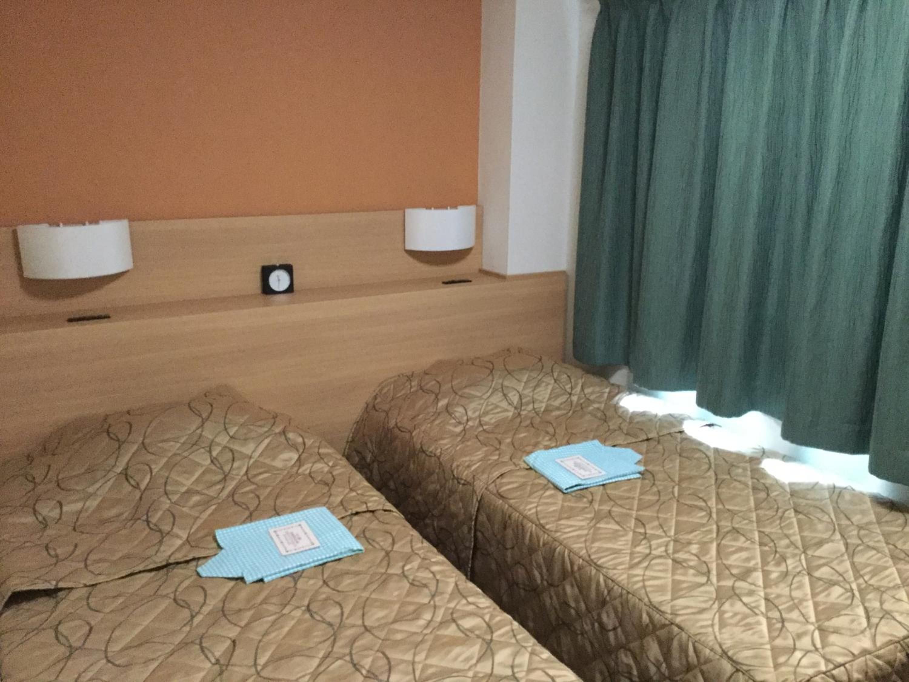 Ein Hotelzimmer mit zwei Betten, einer Uhr und einem Fenster mit Vorhängen.
