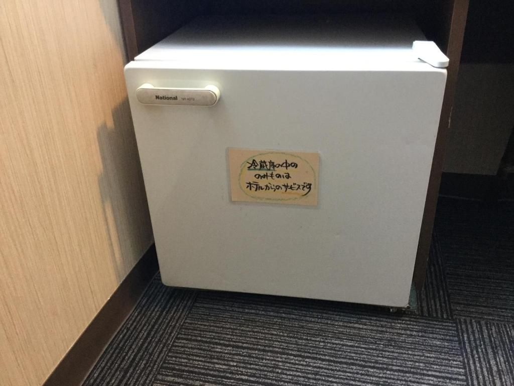 A white refrigerator with a sign on it, located in a room with a carpeted floor and wooden walls.