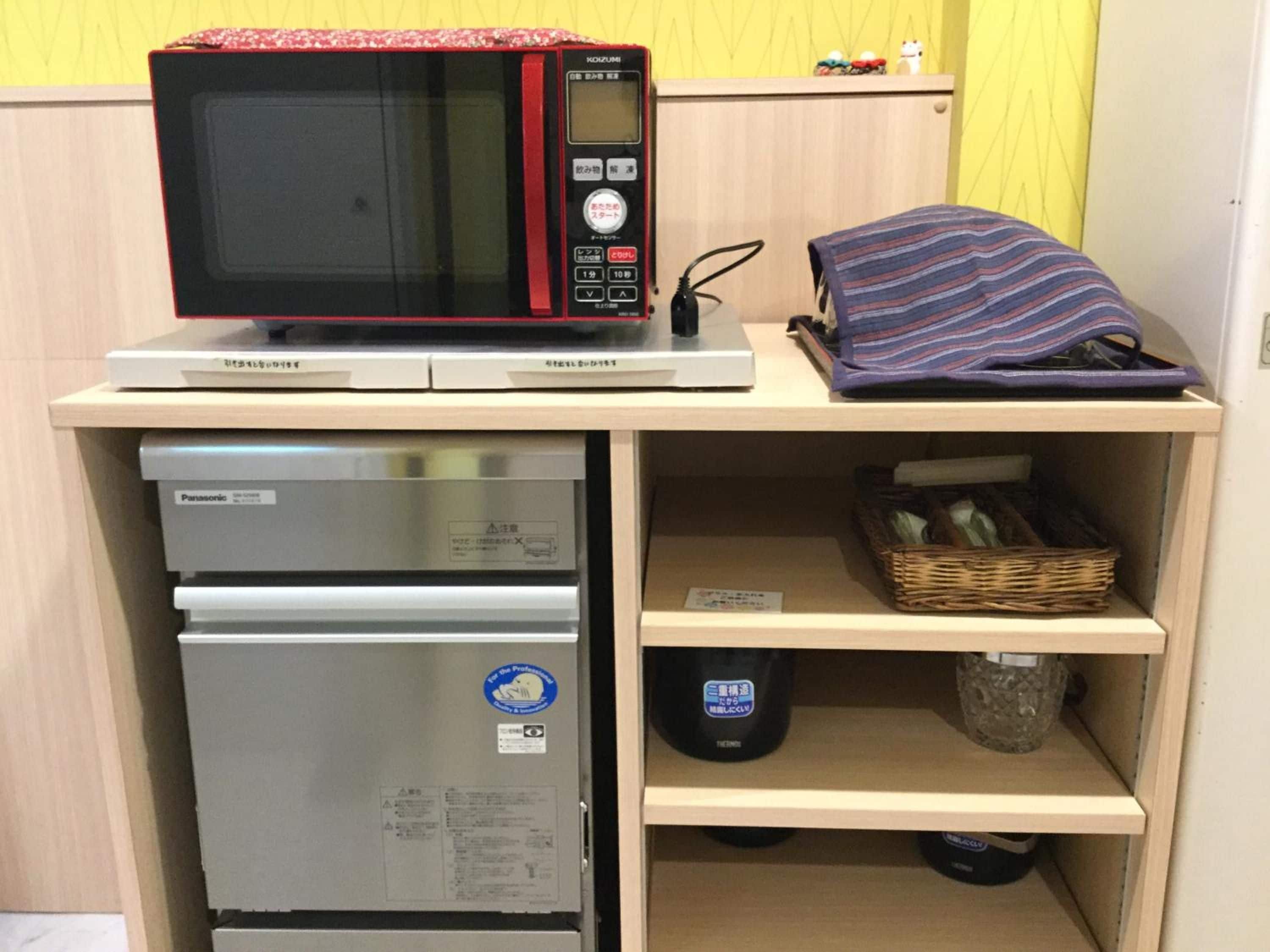 A compact kitchenette with a microwave, refrigerator, and a shelf with a basket and a bag.