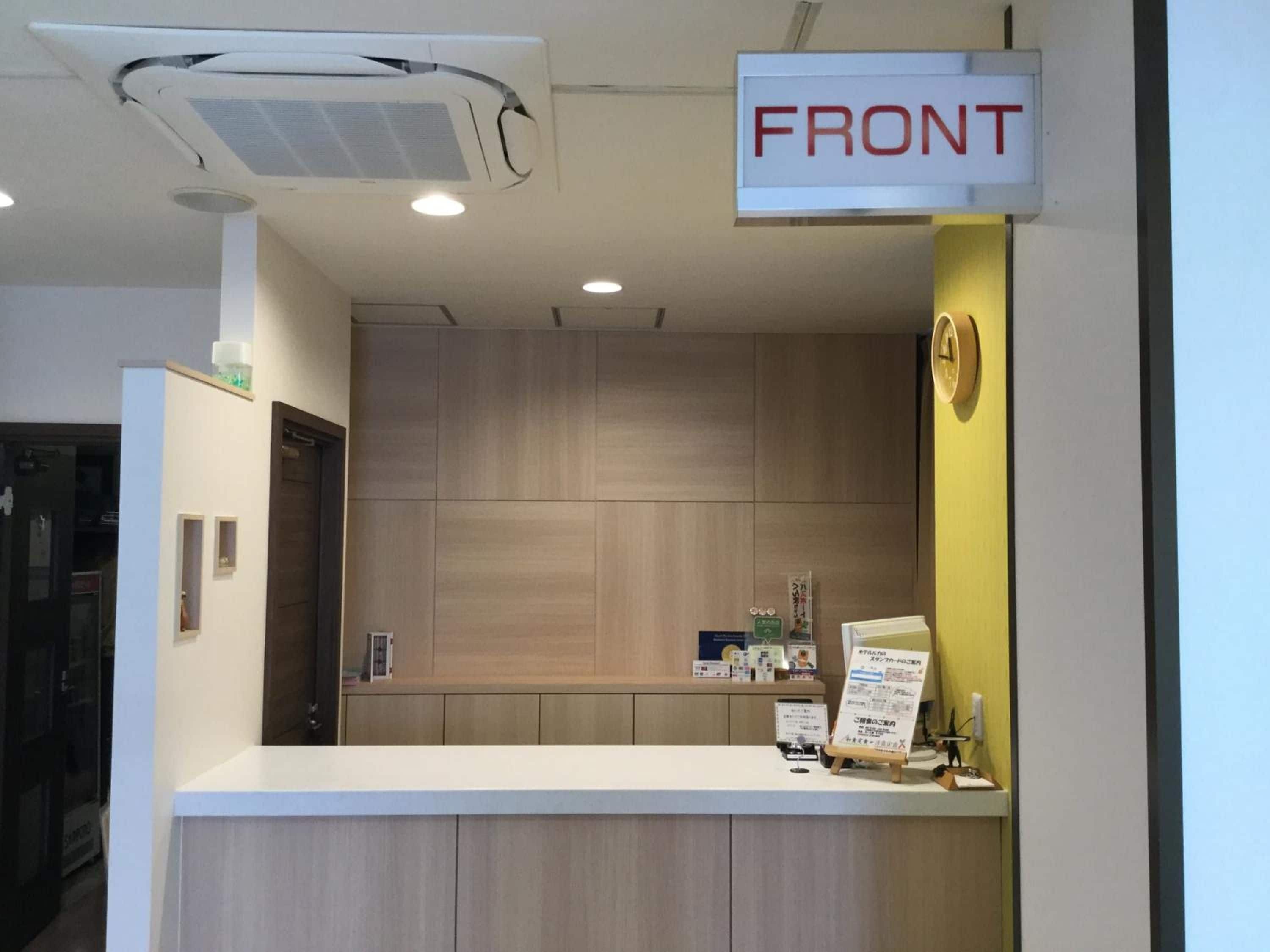 A reception desk with a sign labeled 'FRONT' above it, a light fixture on the ceiling, and a wooden panel wall in the background.