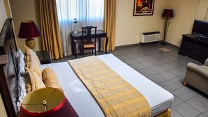 A hotel room with a bed, a desk, a chair, a television, and a lamp. - Victoria Hotel (San Pedro Sula)