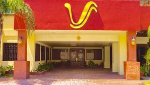 A building entrance with a red facade, a yellow logo, and a brick entrance. - Victoria Hotel (San Pedro Sula)