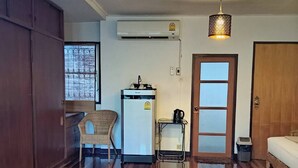 Una habitación con cama, escritorio y silla, refrigerador, aire acondicionado y una puerta.