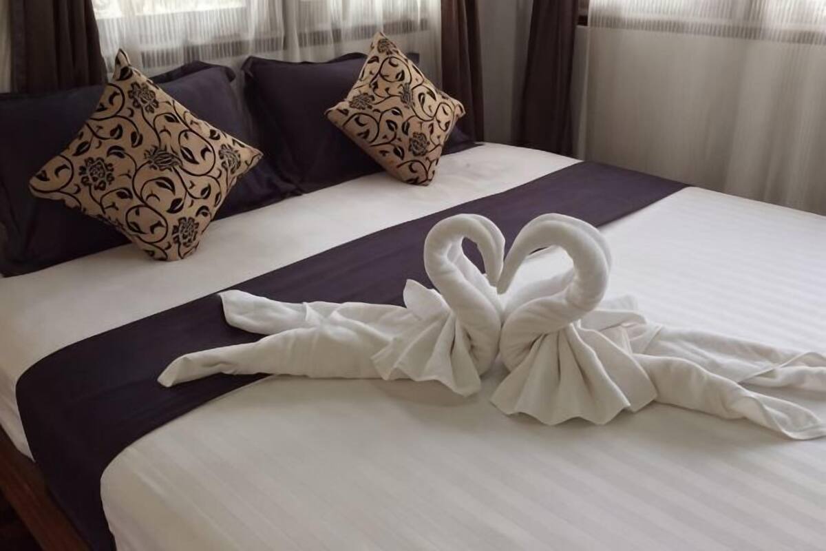 A neatly made bed with a towel arranged in a swan shape, dark bedding, and patterned pillows.