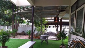Un patio techado con césped artificial, un banco de madera, una mesa de metal y plantas en macetas.