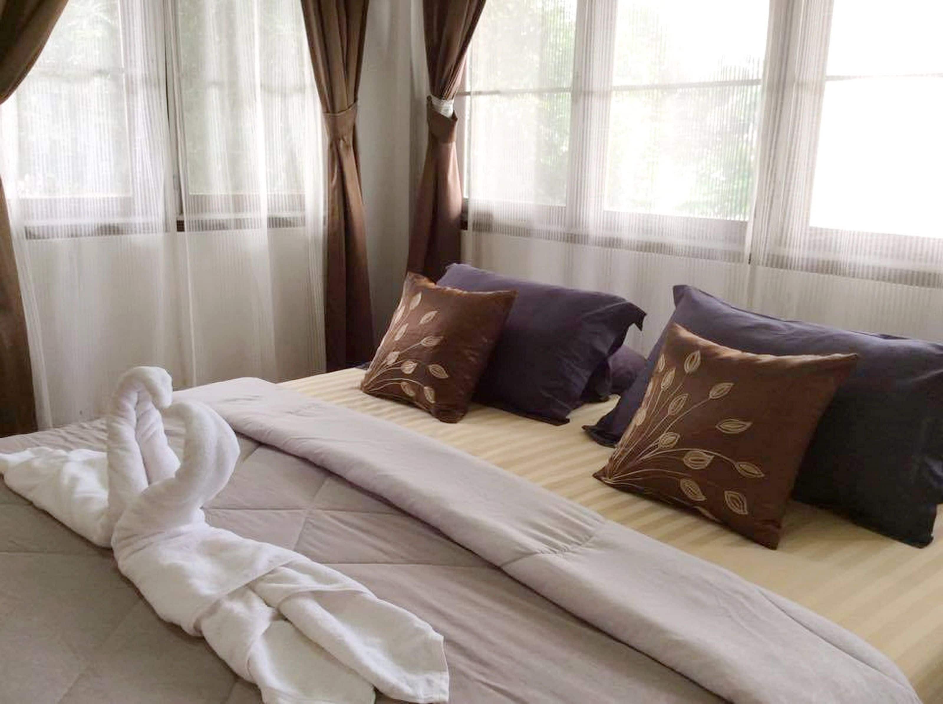 A neatly made bed with a white comforter and a brown blanket, accompanied by several pillows in shades of brown and purple.