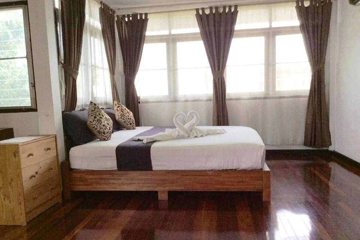 A neatly made bed with a heart-shaped towel arrangement, a wooden nightstand, and a window with curtains.