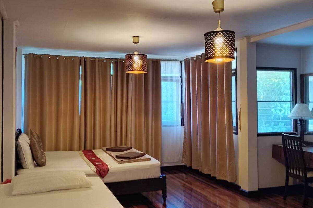 A hotel room with a large bed, two bedside tables, a desk with a chair, and a window with curtains.