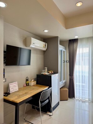 A modern room with a flat-screen TV, air conditioning, a small kitchenette, a wooden desk, and a window with curtains. - Le Neuf Nakorn Lampang (Lampang)