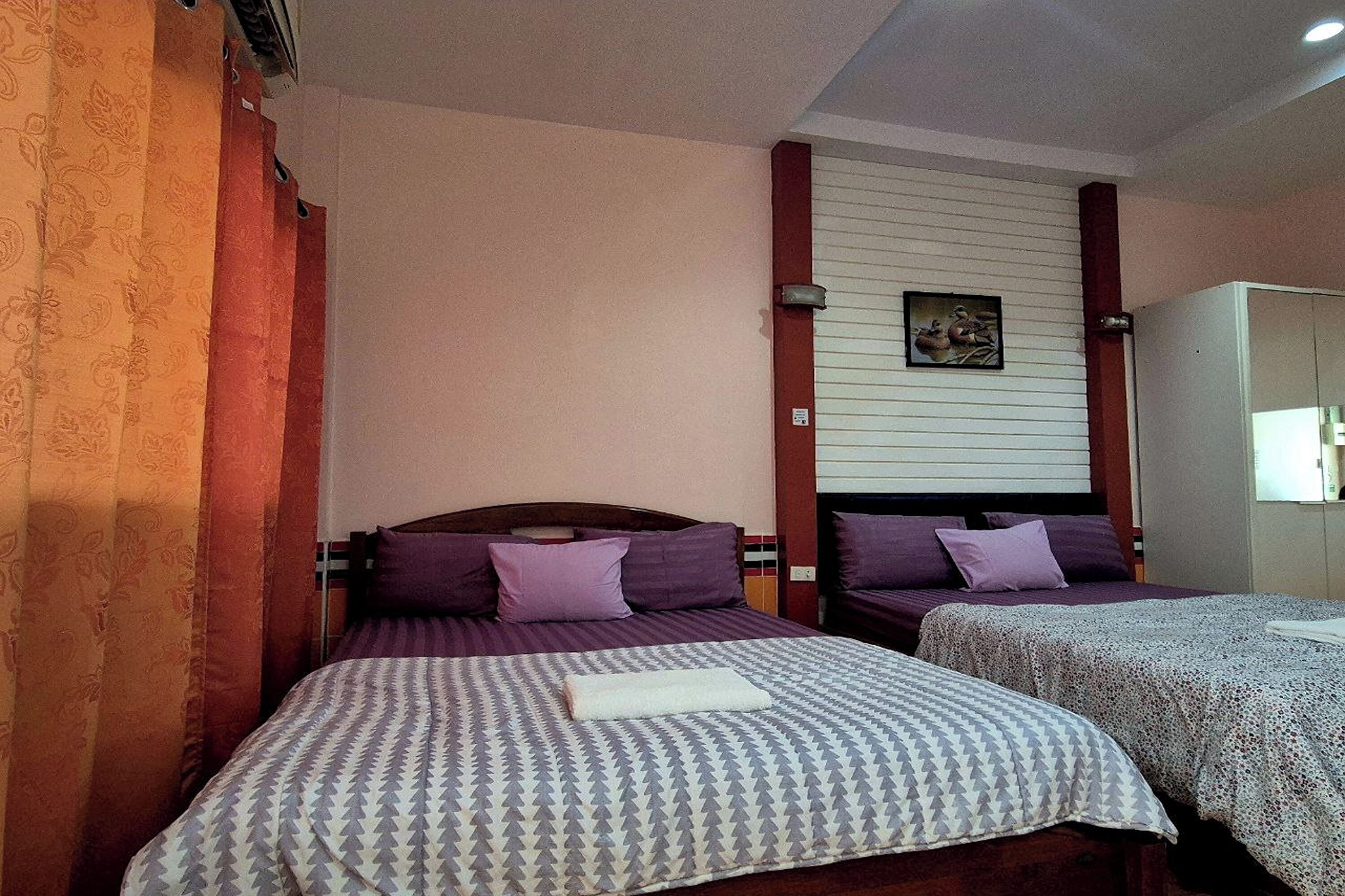 A hotel room with two beds, each with patterned bedding and pillows, a wooden headboard, a wall-mounted artwork, and a wardrobe.