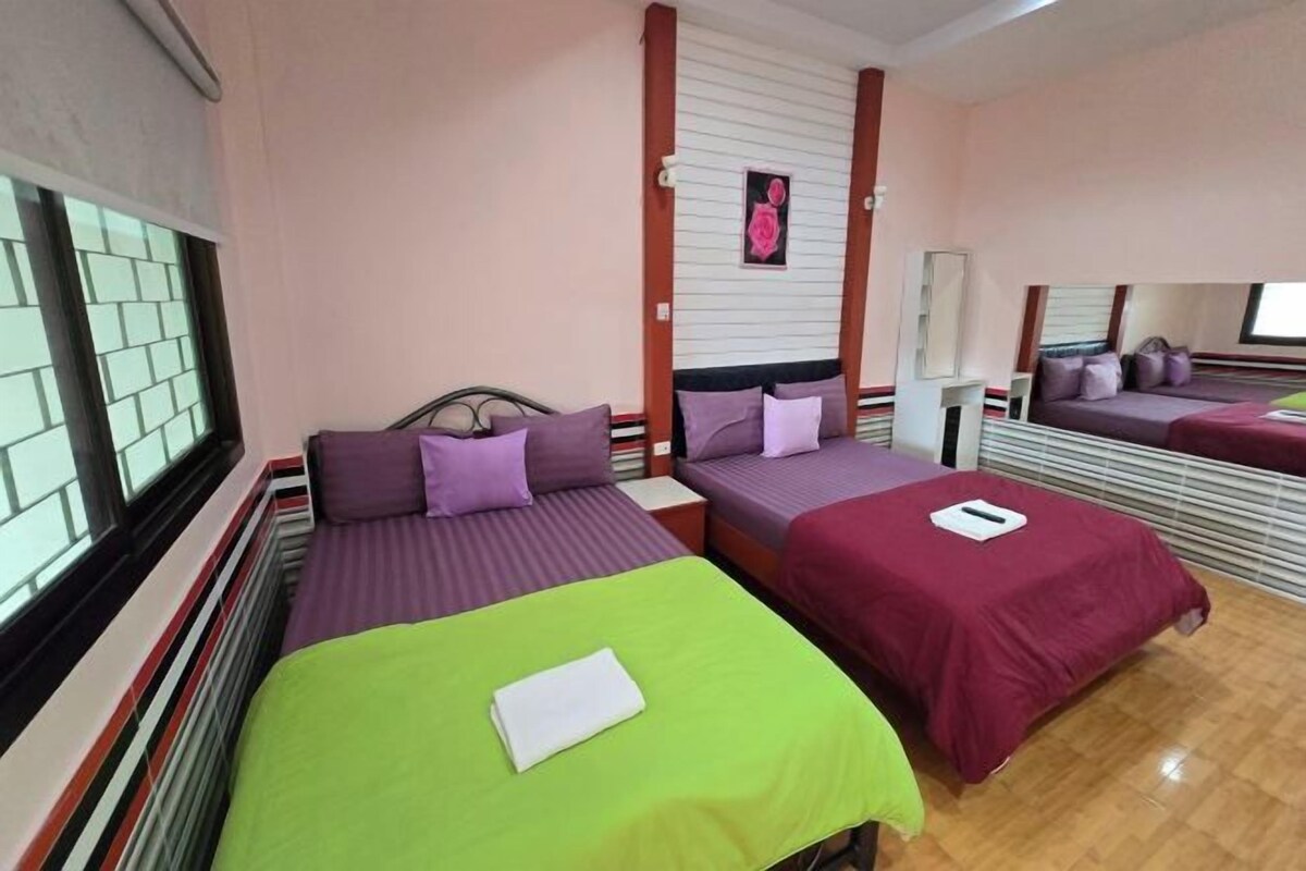 A hotel room with two beds, each with a different colored bedspread, a window with blinds, and a mirror on the wall.