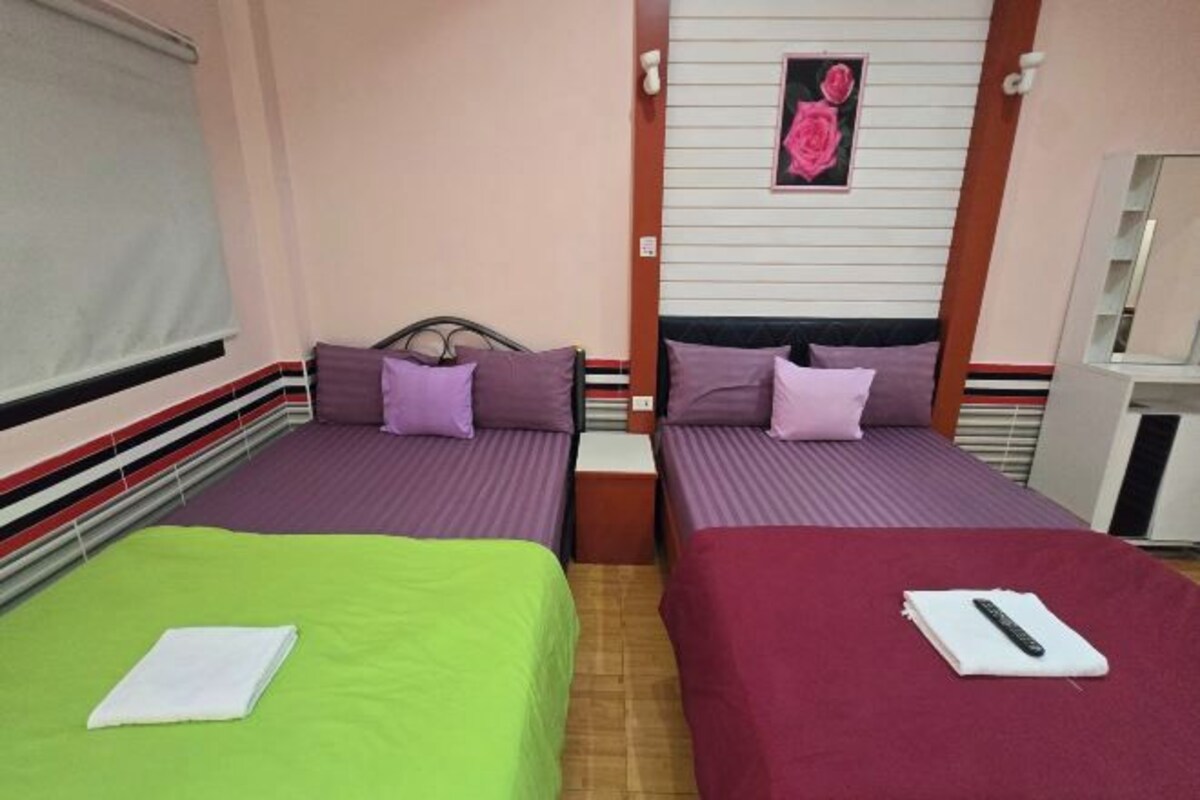A hotel room with two single beds, each with a pillow and a blanket. There is a small table between the beds, and a wall-mounted TV above it.