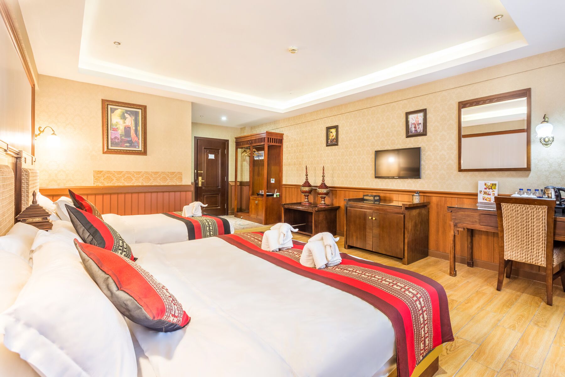 A hotel room with two beds, a desk, a television, and a reception area.