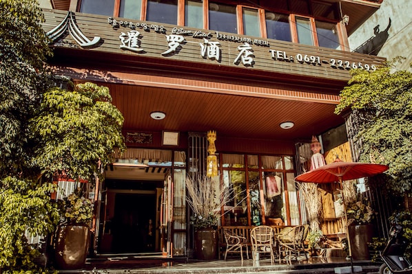 A hotel entrance with a sign, outdoor seating, and potted plants.