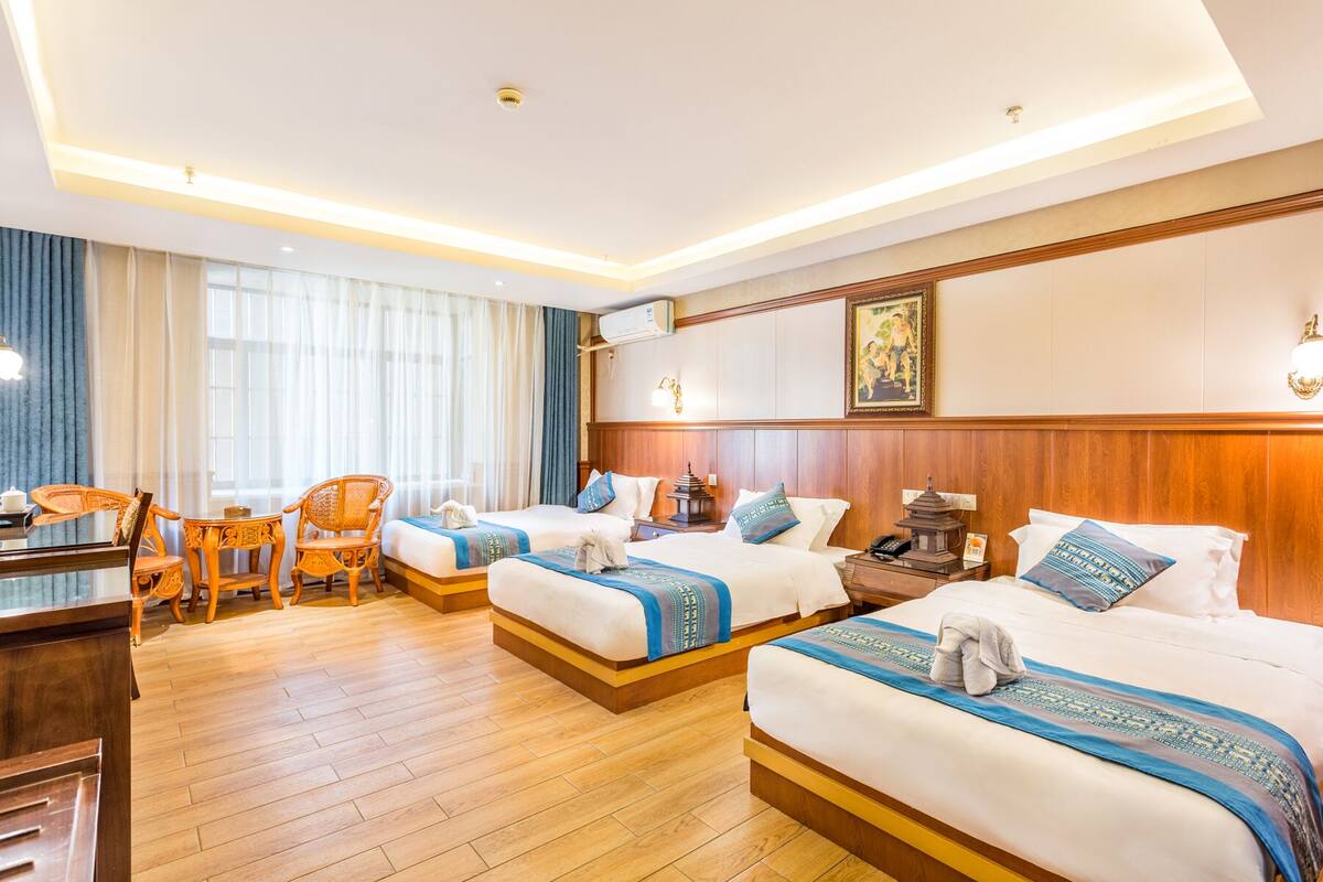 A hotel room with three beds, a desk, and a chair.