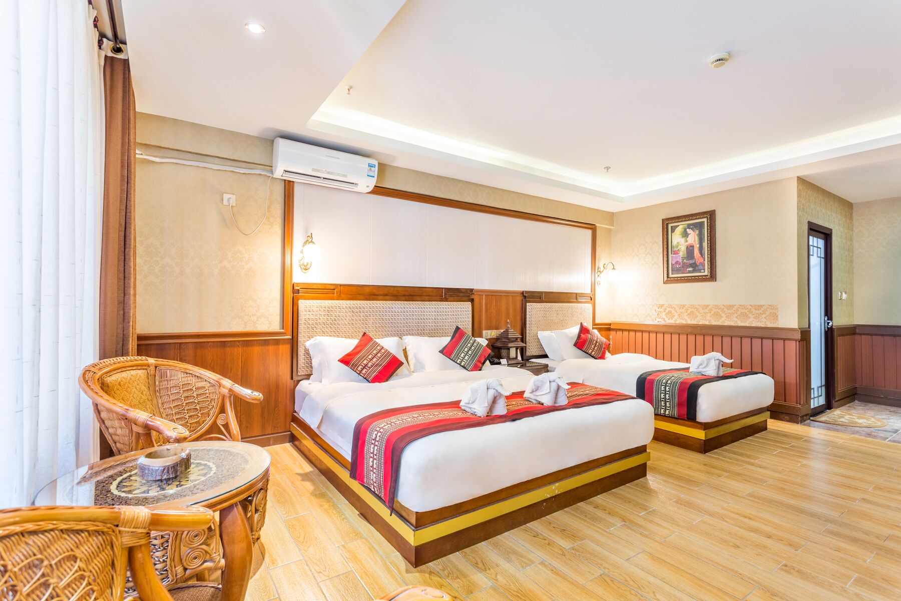 A hotel room with two beds, a sitting area with a chair, a small table, and an air conditioning unit.