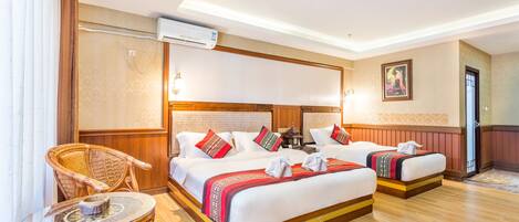 A hotel room with two beds, a sitting area with a chair, a small table, and an air conditioning unit.