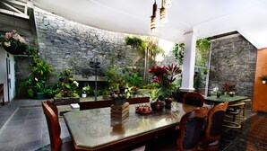 A dining area with a stone wall, wooden furniture, and potted plants. - Fora Guest House Taman Lingkar (Bandung)