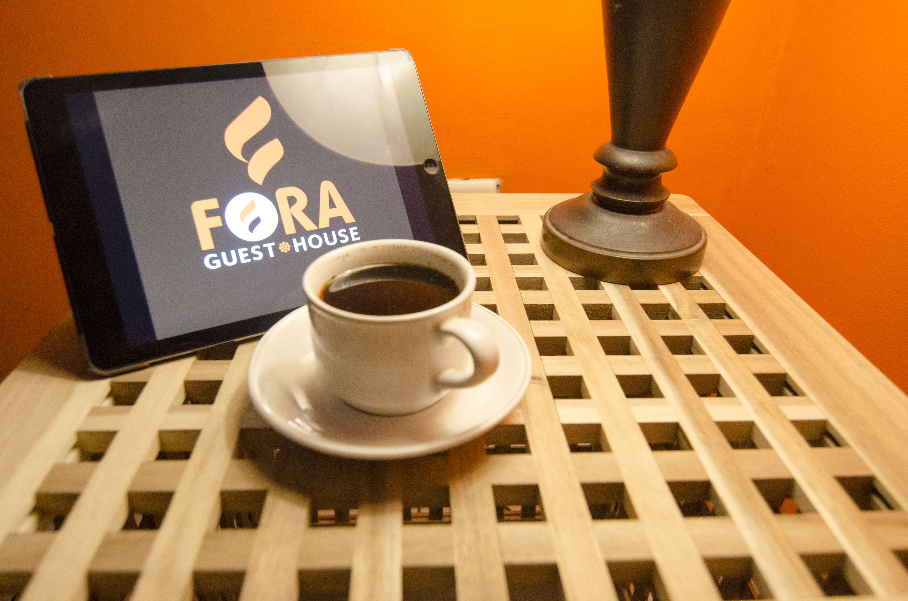 Una tableta que muestra el logotipo de "FORA GUEST HOUSE" junto a una taza de café sobre una bandeja de madera.
